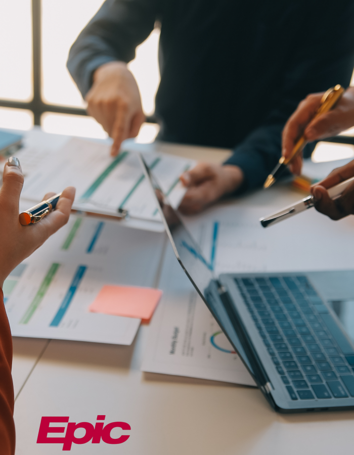 team collaboration with data sheets, laptops, pens, and EPIC logo in the corner